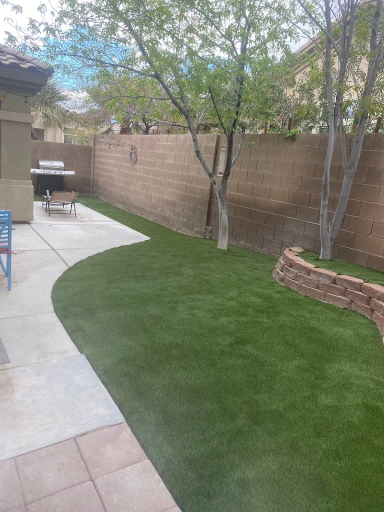 Backyard artificial turf installation with mature trees and a stone retaining wall
